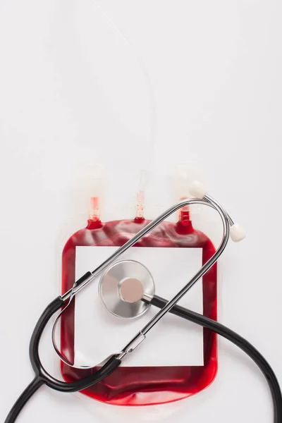 Vista superior del paquete de donación de sangre con etiqueta en blanco y estetoscopio aislado en blanco - foto de stock