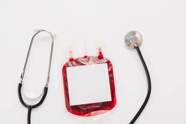 Ansicht der Blutspendeverpackung mit Blanko-Etikett und Stethoskop isoliert auf weiß — Stockfoto