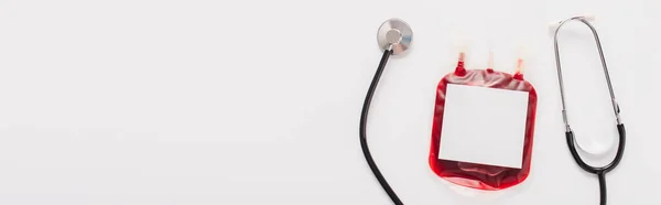 Top view of blood donation package with blank label and stethoscope isolated on white, panoramic shot — Stock Photo