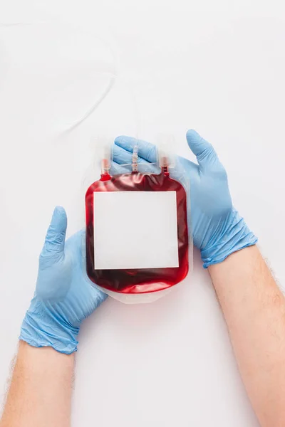 Vista recortada del médico que sostiene el paquete de donación de sangre con etiqueta en blanco sobre fondo blanco - foto de stock