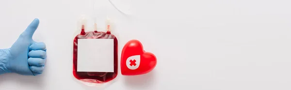 Ausgeschnittene Ansicht des Arztes zeigt Daumen nach oben in der Nähe von Blutpaket und rotem Herz auf weißem Hintergrund, Panoramaaufnahme — Stockfoto