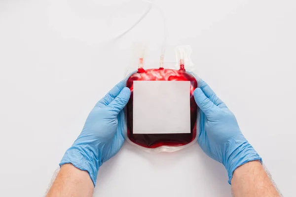 Vista recortada del médico que sostiene el paquete de donación de sangre con etiqueta en blanco sobre fondo blanco - foto de stock