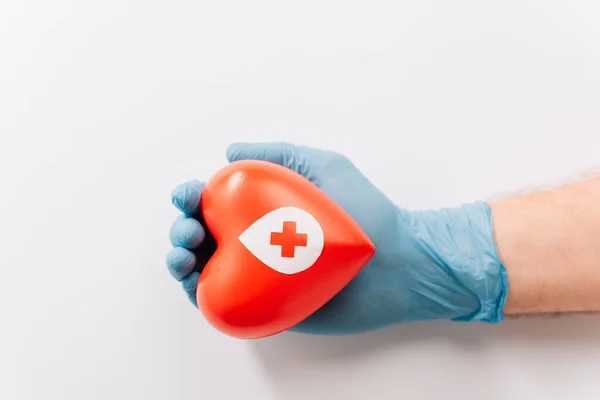Ausgeschnittene Ansicht der männlichen Hand in Latex-Handschuh mit rotem Herz auf weißem, Blutspendekonzept — Stockfoto