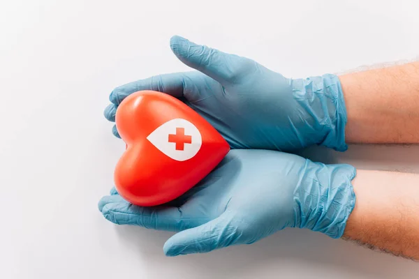 Vista recortada de las manos masculinas en guantes de látex con corazón rojo sobre blanco, concepto de donación de sangre - foto de stock