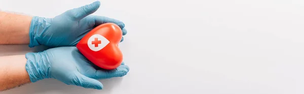 Vista recortada de las manos masculinas en guantes de látex con corazón rojo sobre blanco, concepto de donación de sangre - foto de stock