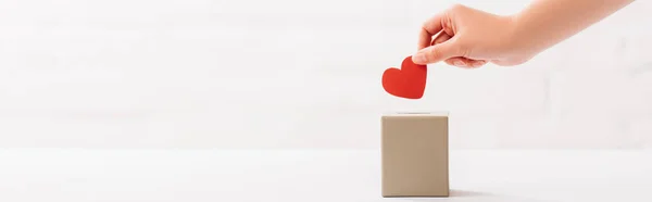 Cropped view of female hand putting red heart in box on white background, donation concept — Stock Photo