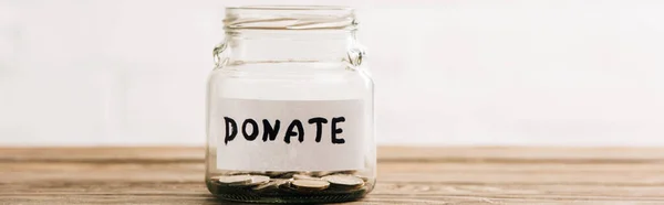 Penny jar with donate lettering on wooden surface on white background, panoramic shot — Stock Photo