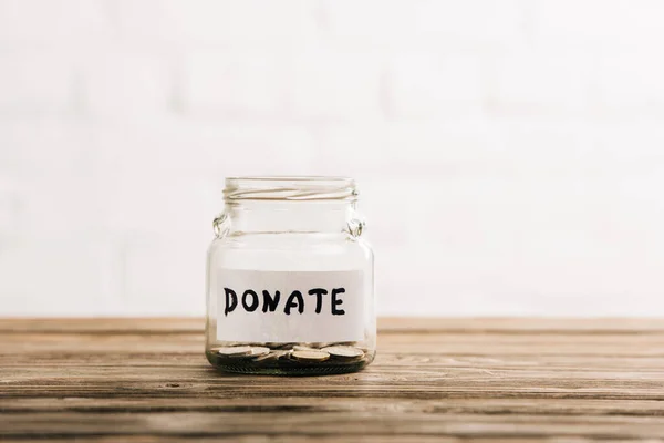 Frasco de centavo con donar letras en la superficie de madera sobre fondo blanco - foto de stock