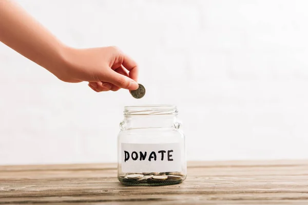 Vista recortada de la mujer poniendo moneda en frasco de penique con donar letras en la superficie de madera sobre fondo blanco - foto de stock