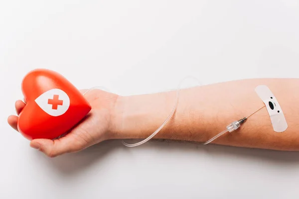 Vista ritagliata della mano maschile con cuore rosso e catetere su bianco, concetto di donazione di sangue — Foto stock