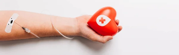 Visão recortada da mão masculina com coração vermelho e cateter em branco, conceito de doação de sangue — Fotografia de Stock