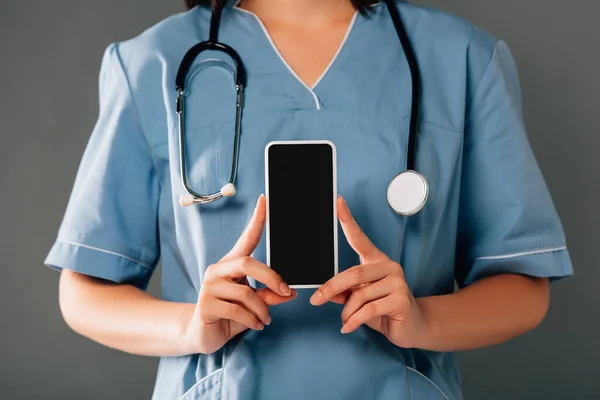 Vista ritagliata del medico con smartphone in possesso di stereoscopio e schermo vuoto isolato sul grigio — Foto stock