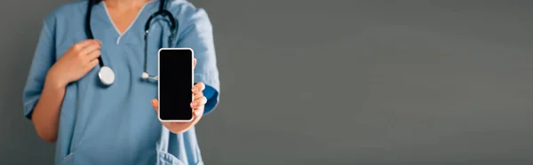 Cropped view of doctor with stereoscope holding smartphone and blank screen isolated on grey, panoramic shot — Stock Photo