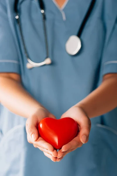 Vista recortada del médico con estereoscopio que sostiene el corazón rojo - foto de stock