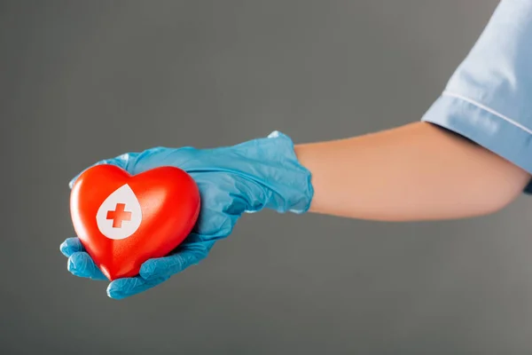 Vista ritagliata del medico che tiene il cuore rosso isolato sul grigio, concetto di donazione di sangue — Foto stock