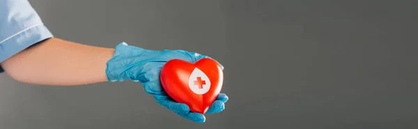 Vista recortada del médico sosteniendo corazón rojo aislado en gris, concepto de donación de sangre - foto de stock