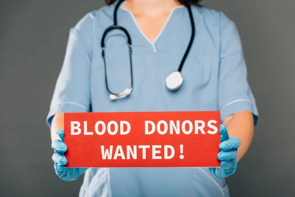 Cropped view of doctor with stereoscope holding red card with blood donors wanted lettering isolated on grey — Stock Photo