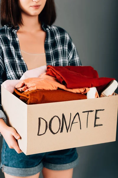 Vista recortada de la caja de espera de la mujer con donar letras y ropa sobre fondo gris - foto de stock