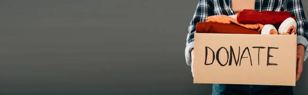Обрезанный вид женщины с коробкой для пожертвований с надписью и одеждой на сером фоне, панорамный снимок — стоковое фото
