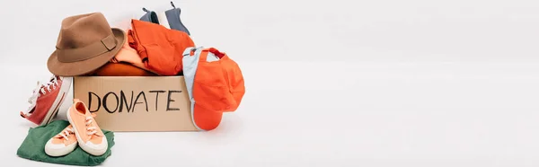 Панорамный снимок картонной коробки с подаренными аксессуарами, одеждой и обувью, изолированной на белом, благотворительная концепция — стоковое фото