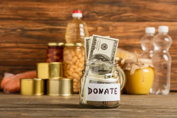 Selective focus of jar with money and donated food on wooden background, charity concept — Stock Photo