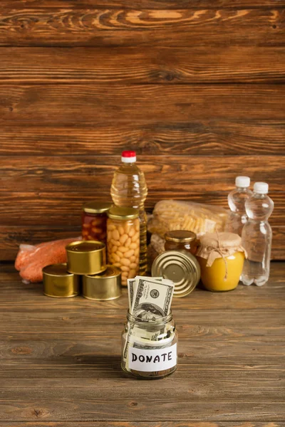 Enfoque selectivo de tarro con dinero y alimentos donados sobre fondo de madera, concepto de caridad - foto de stock