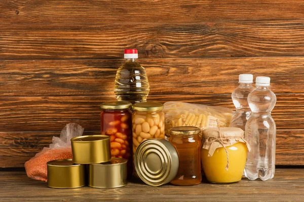 Groats cerca del agua, aceite, alimentos enlatados y miel sobre fondo de madera, concepto de caridad - foto de stock