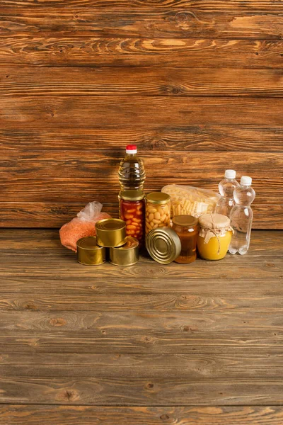 Groats cerca del agua, aceite, alimentos enlatados y miel sobre fondo de madera, concepto de caridad - foto de stock