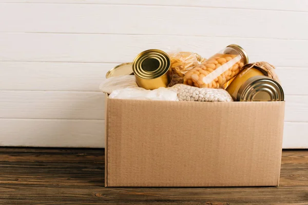 Caja de cartón con alimentos donados sobre fondo de madera, concepto de caridad - foto de stock