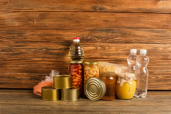 Groats cerca del agua, aceite, alimentos enlatados y miel sobre fondo de madera, concepto de caridad - foto de stock