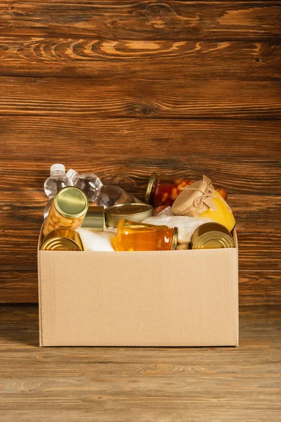 Cardboard box with donated food on wooden background, charity concept — Stock Photo