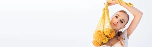 Модная женщина позирует с цитрусовыми фруктами в струнном мешке изолированы на белом, панорамный снимок — стоковое фото