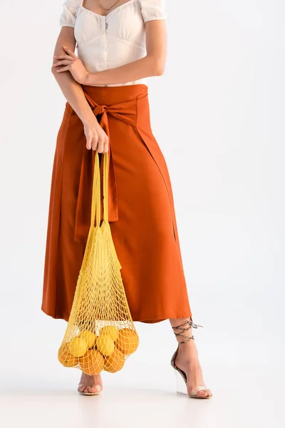 Cropped view of fashionable woman posing with citrus fruits in string bag isolated on white — Stock Photo