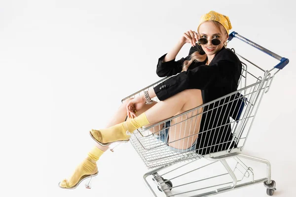 Mulher na moda em roupa preta e amarela posando no carrinho de compras isolado no branco — Fotografia de Stock