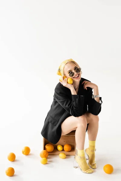 Mujer de moda posando en caja de madera cerca de cítricos dispersos sobre fondo blanco — Stock Photo