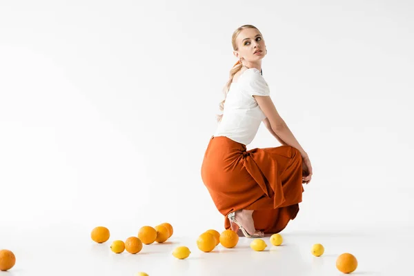 Side view of elegant blonde woman posing near citrus fruits on white background — Stock Photo