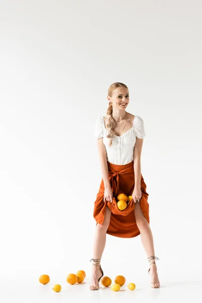 Веселая элегантная блондинка позирует с цитрусовыми в юбке на белом фоне — стоковое фото