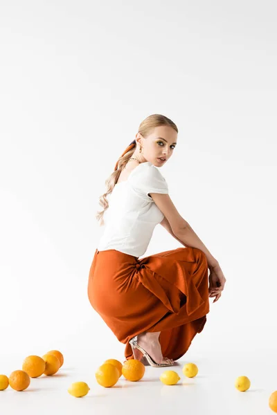 Side view of elegant blonde woman posing near citrus fruits on white background — Stock Photo