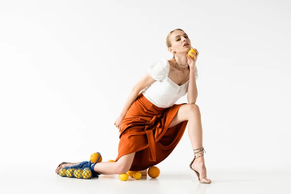 Mulher loira elegante posando com saco de cordas perto de frutas cítricas espalhadas no fundo branco — Fotografia de Stock