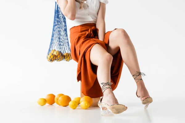 Vista cortada de mulher elegante posando com saco de cordas perto de frutas cítricas espalhadas no fundo branco — Fotografia de Stock