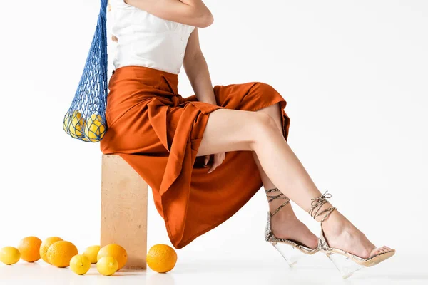 Vista ritagliata di donna elegante in posa con borsa stringa vicino agli agrumi sparsi su sfondo bianco — Foto stock