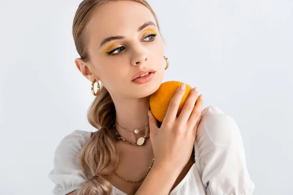 Mujer rubia elegante posando con naranja y mirando hacia otro lado aislado en blanco - foto de stock