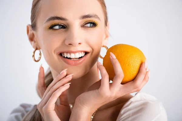 Cheerful elegant blonde woman holding orange and looking away isolated on white — Stock Photo