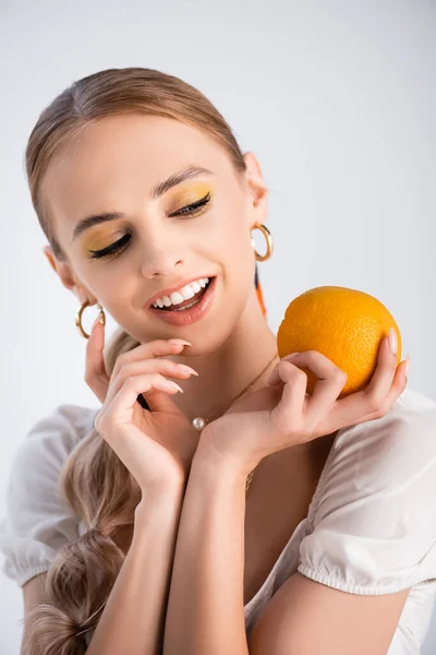 Elegante donna bionda sorridente mentre posa con arancione isolato su bianco — Foto stock