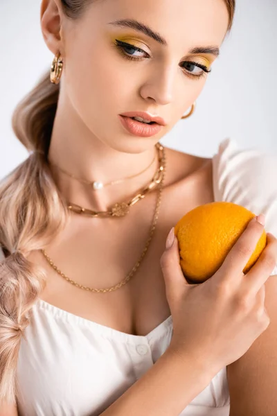 Elegant blonde woman posing with orange and looking away isolated on white — Stock Photo