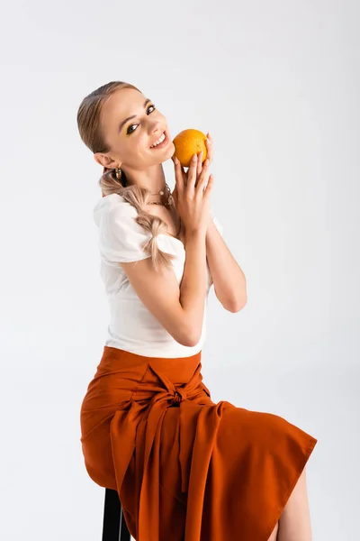 Cheerful blonde woman posing with orange isolated on white — Stock Photo