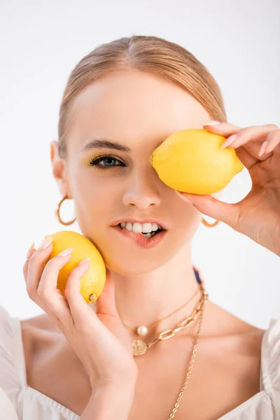 Élégante femme blonde posant avec des citrons et la lèvre mordante isolé sur blanc — Photo de stock