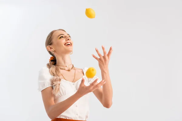 Mujer rubia haciendo malabares con limones amarillos aislados en blanco - foto de stock