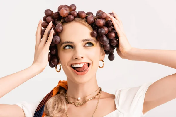 Rustic blonde woman holding grapes on head and showing tongue isolated on white — Stock Photo