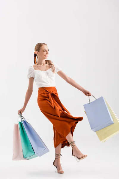 Vue pleine longueur de femme élégante marchant avec des sacs à provisions sur blanc — Photo de stock